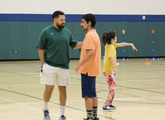 Coach Gonzalez teaching Partners PE student how to throw a football. 
